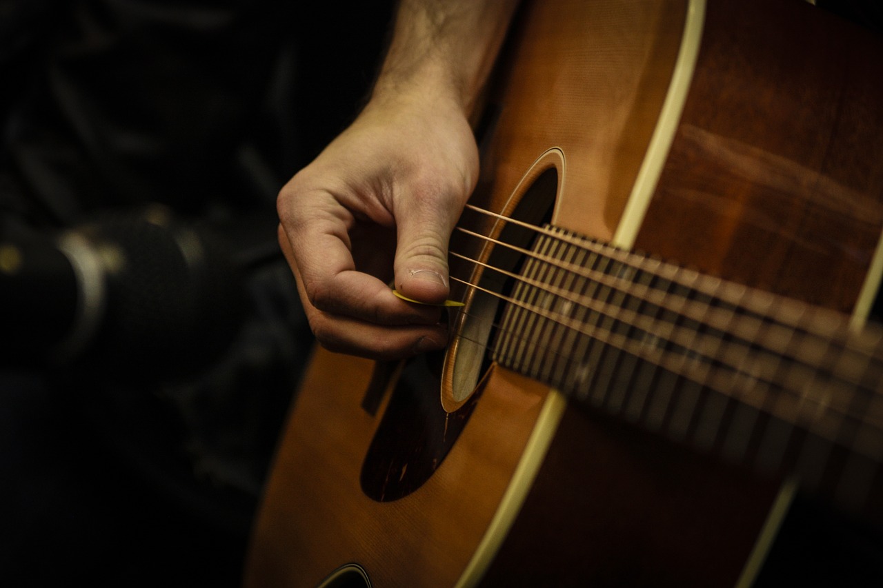 A imagem mostra uma pessoa tocando violão. É possível ver apenas sua mão segurando uma palheta..