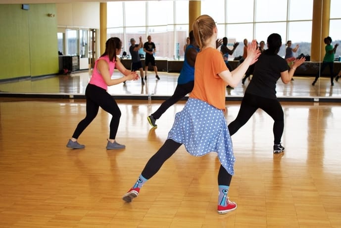 A imagem mostra algumas pessoas frente a um espelho, em uma aula de dança.