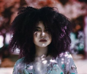 A imagem mostra uma moça com cabelos afro na cor marsala.