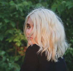 A imagem mostra uma moça com o cabelo platinado, cortado na altura dos ombros no estilo long bob