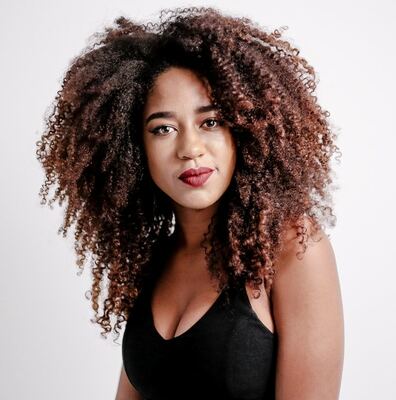 A imagem mostra uma moça negra, com cabelo afro longo, cortado em camadas, que conferem volume e movimento.