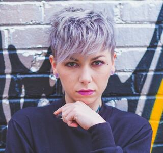 A imagem mostra uma moça com um cabelo lilás cortado no estilo pixie cut.