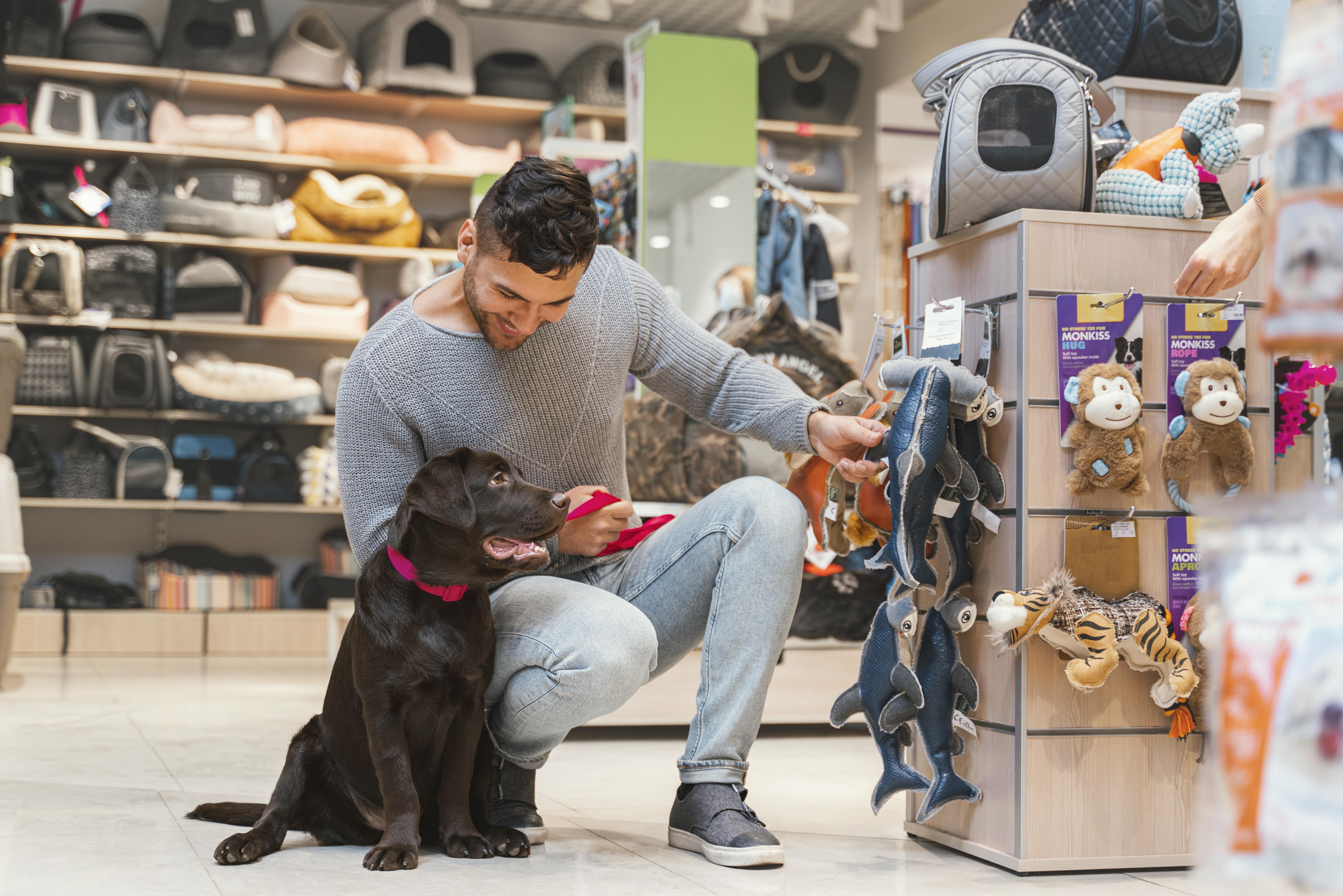 Homem agachado ao lado de seu cachorro olhando produtos de petshop.