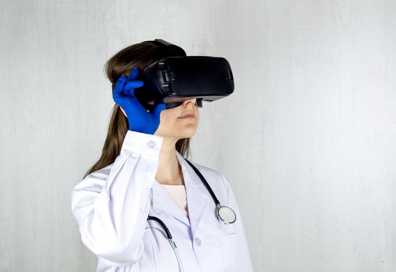 A imagem descreve uma doutora trajando jaleco branco e usando óculos de realidade virtual.