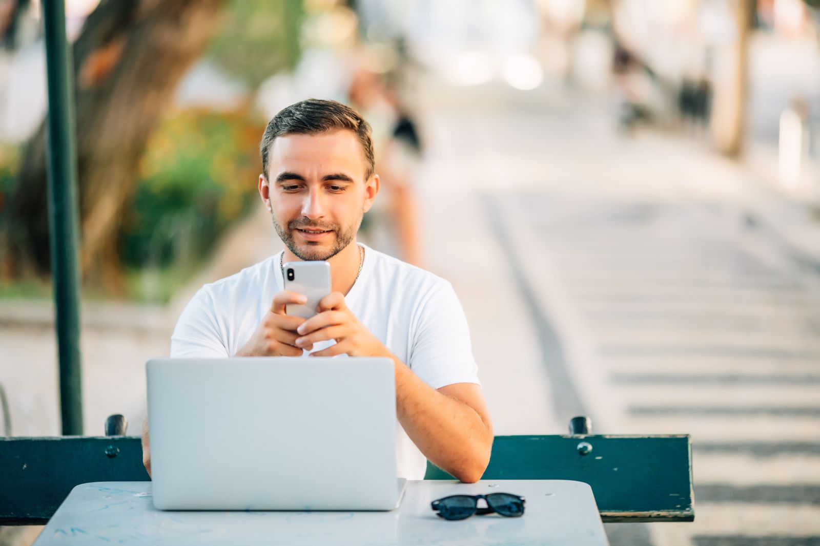 Um homem sentado ao redor de uma mesa com um laptop segura um smartphone.