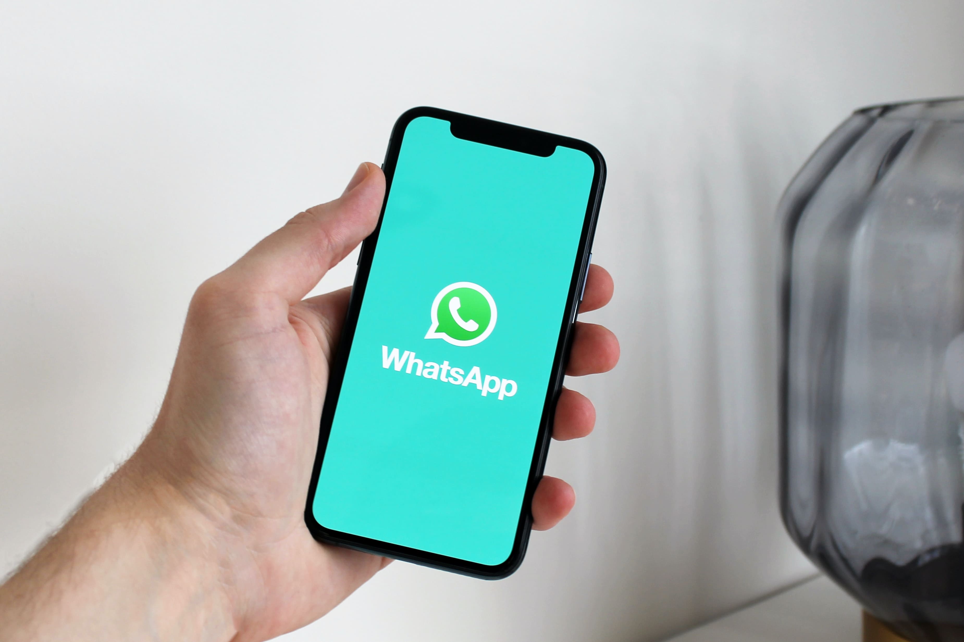 Uma mão segurando um celular que exibe o logo do aplicativo Whatsapp.